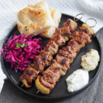 plate with lamb shish kebab, red cabbage, bread and sauces