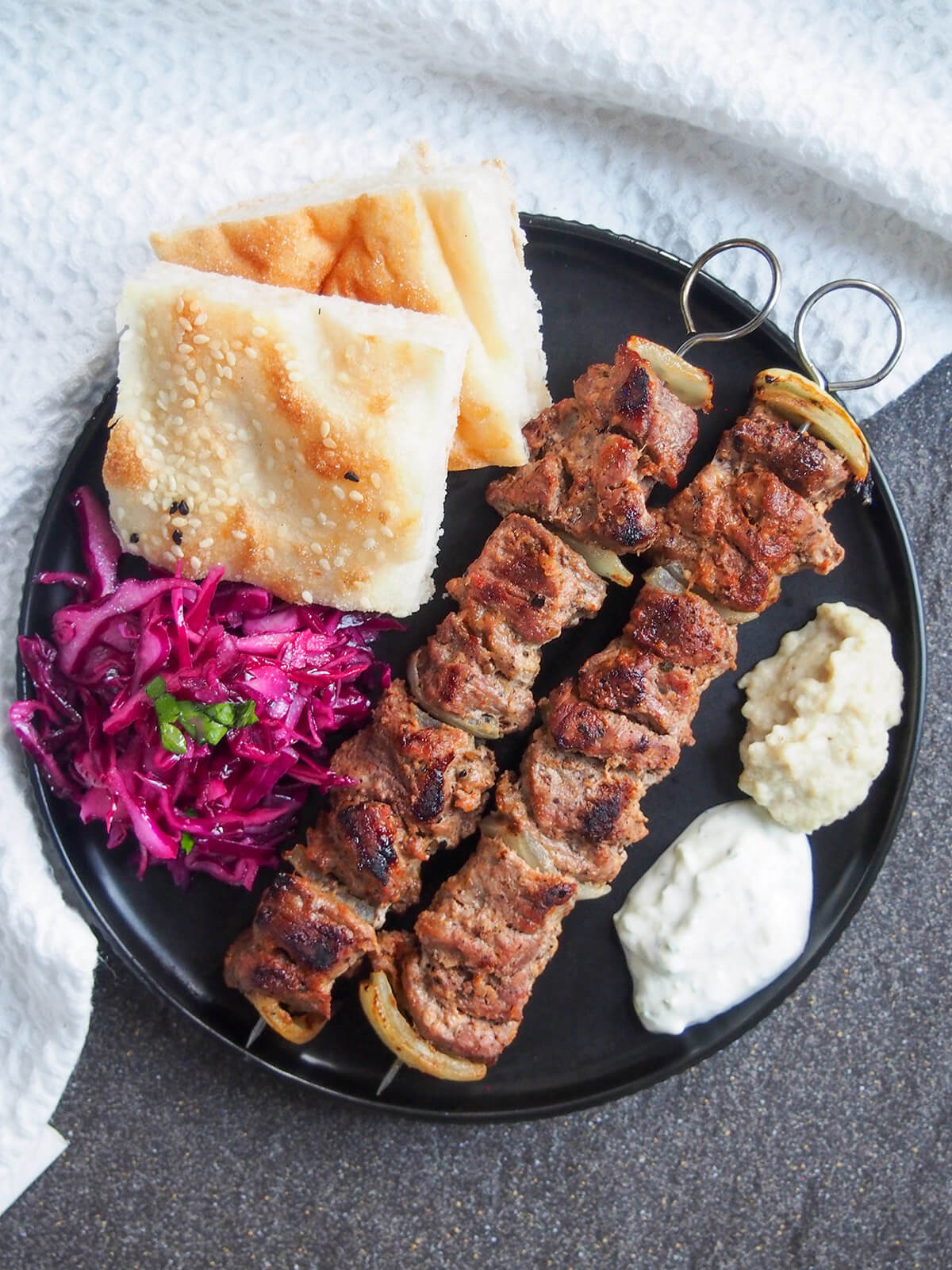 plate of lamb shish kebabs, bread, read cabbage and sauces from overhead