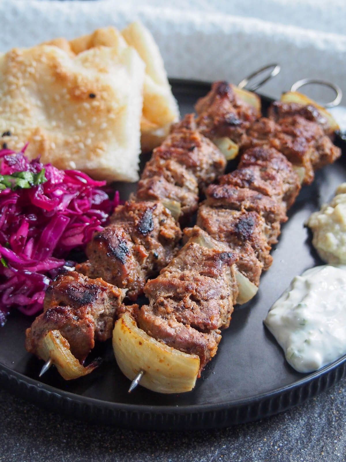 two lamb shish kebabs on plate with sides partly in view wither side