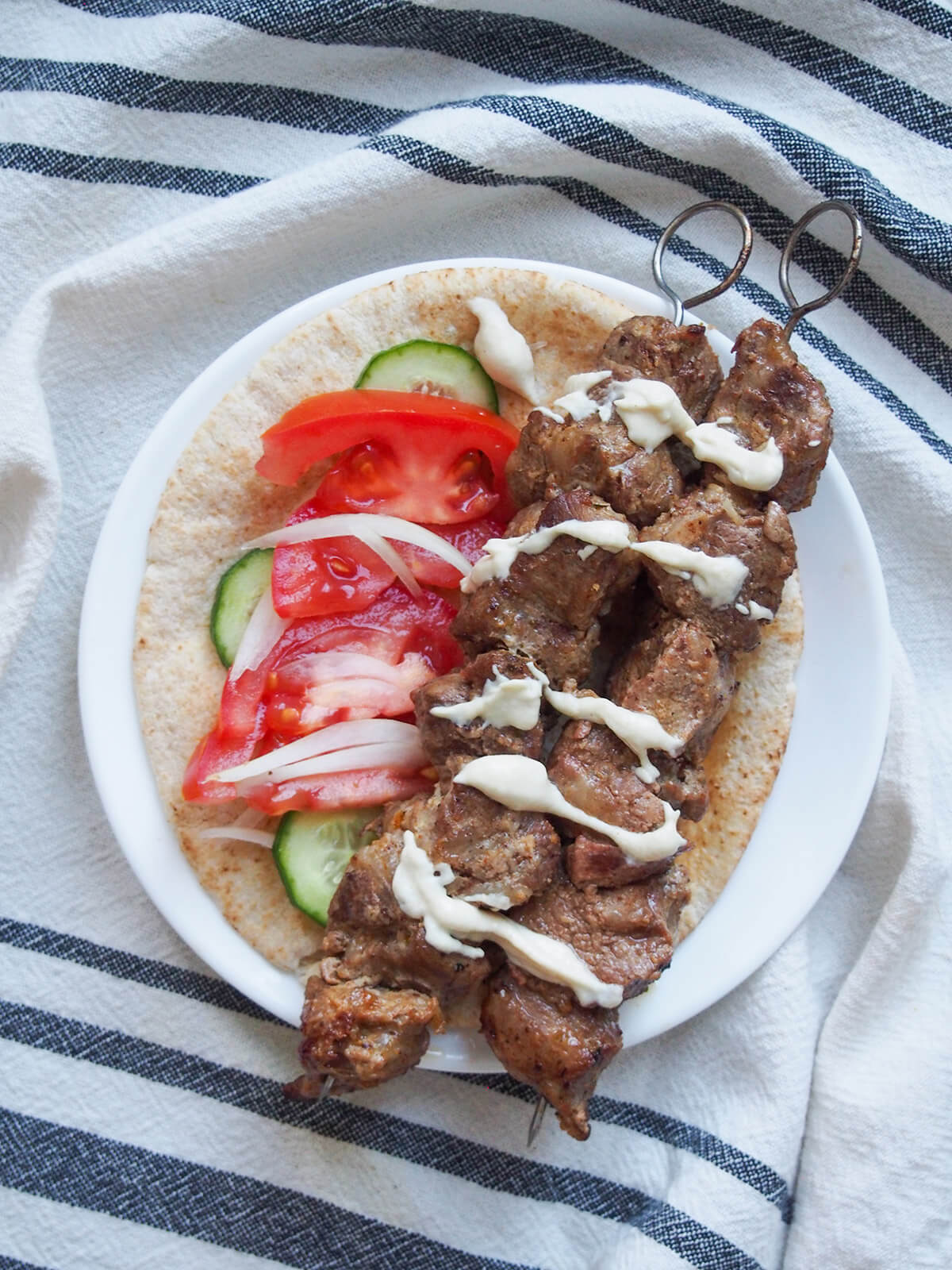 two skewers of lamb shish kebab on pita with tomato salad to side