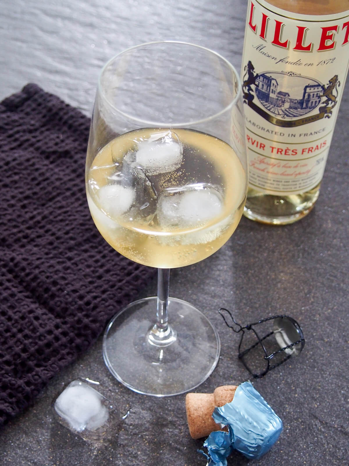 glass of lillet spritz with ice in it and bottle behind