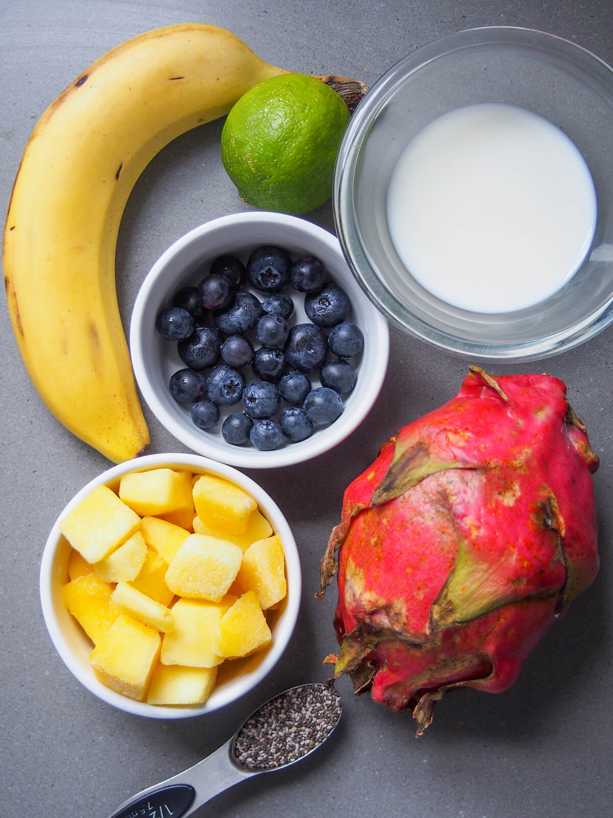 bowls with fruit, milk with banana, lime and dragonfruit to side and chia seeds below