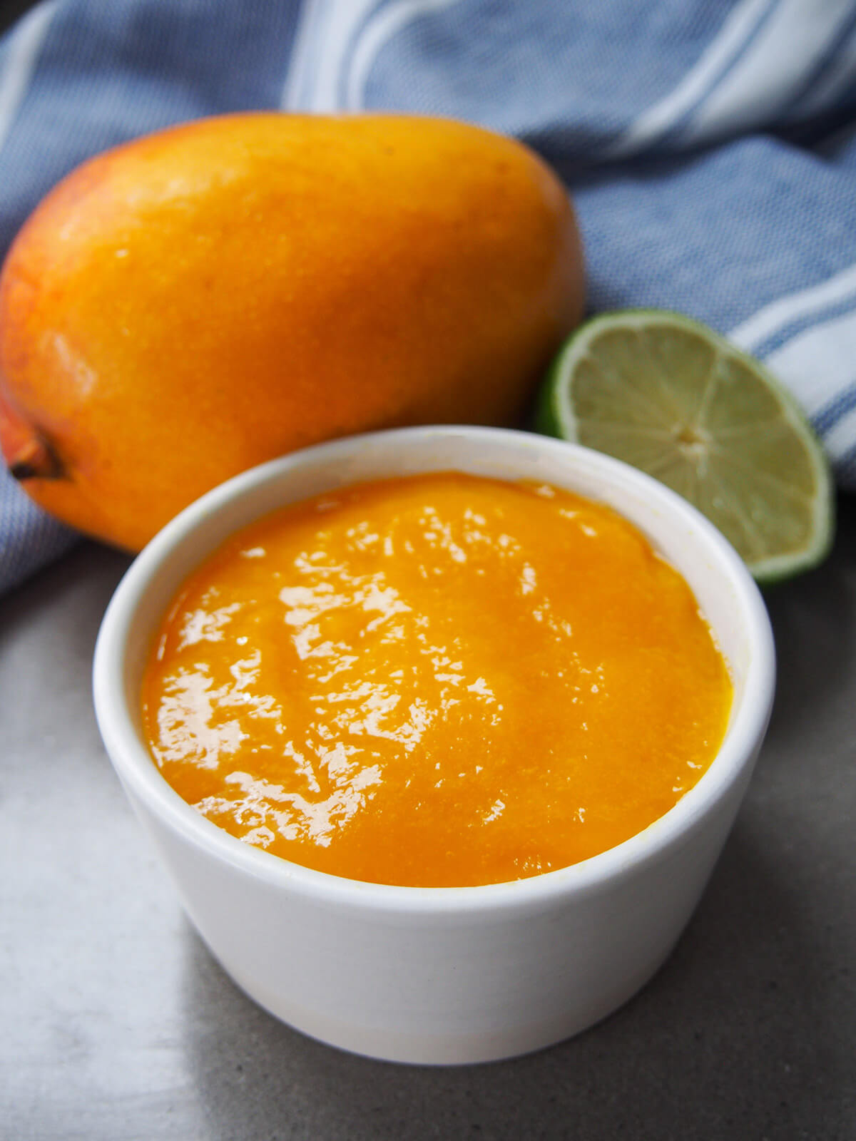 bowl of mango sauce with mango and lime behind
