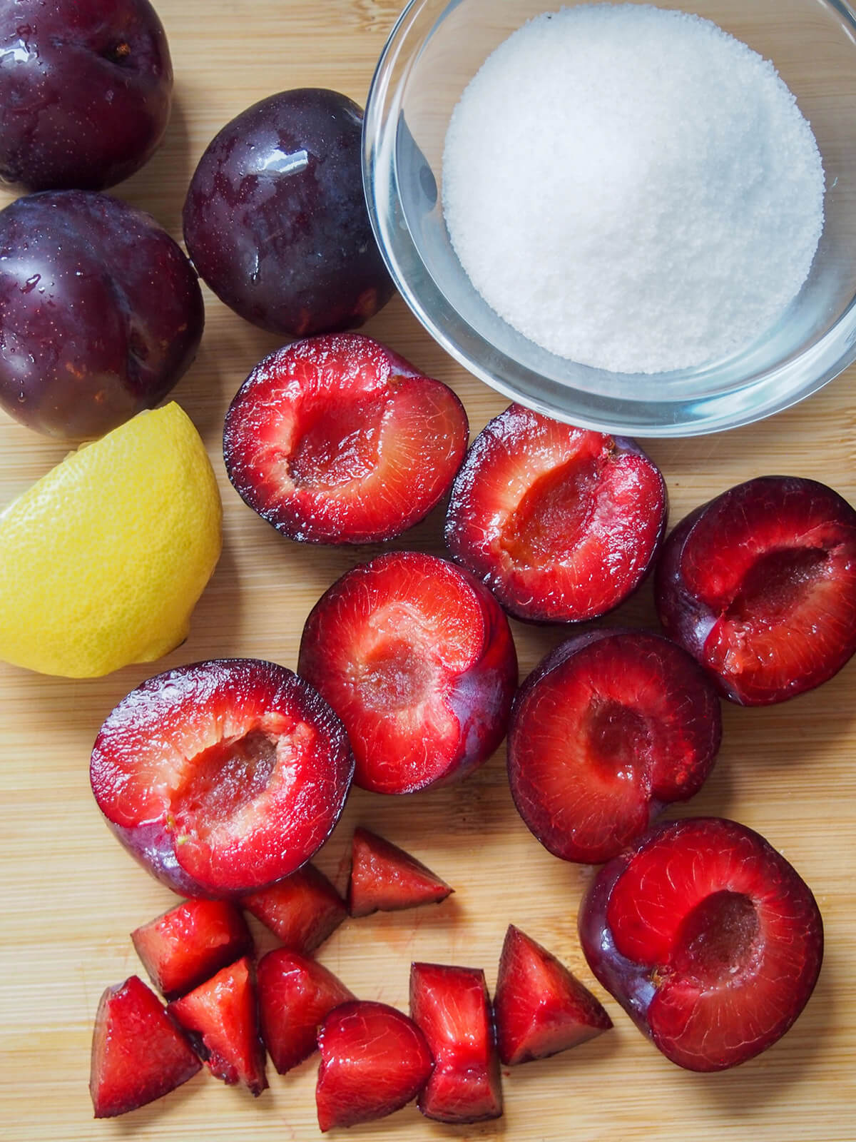 halved and chopped plums with bowl of sugar to side and part lemon