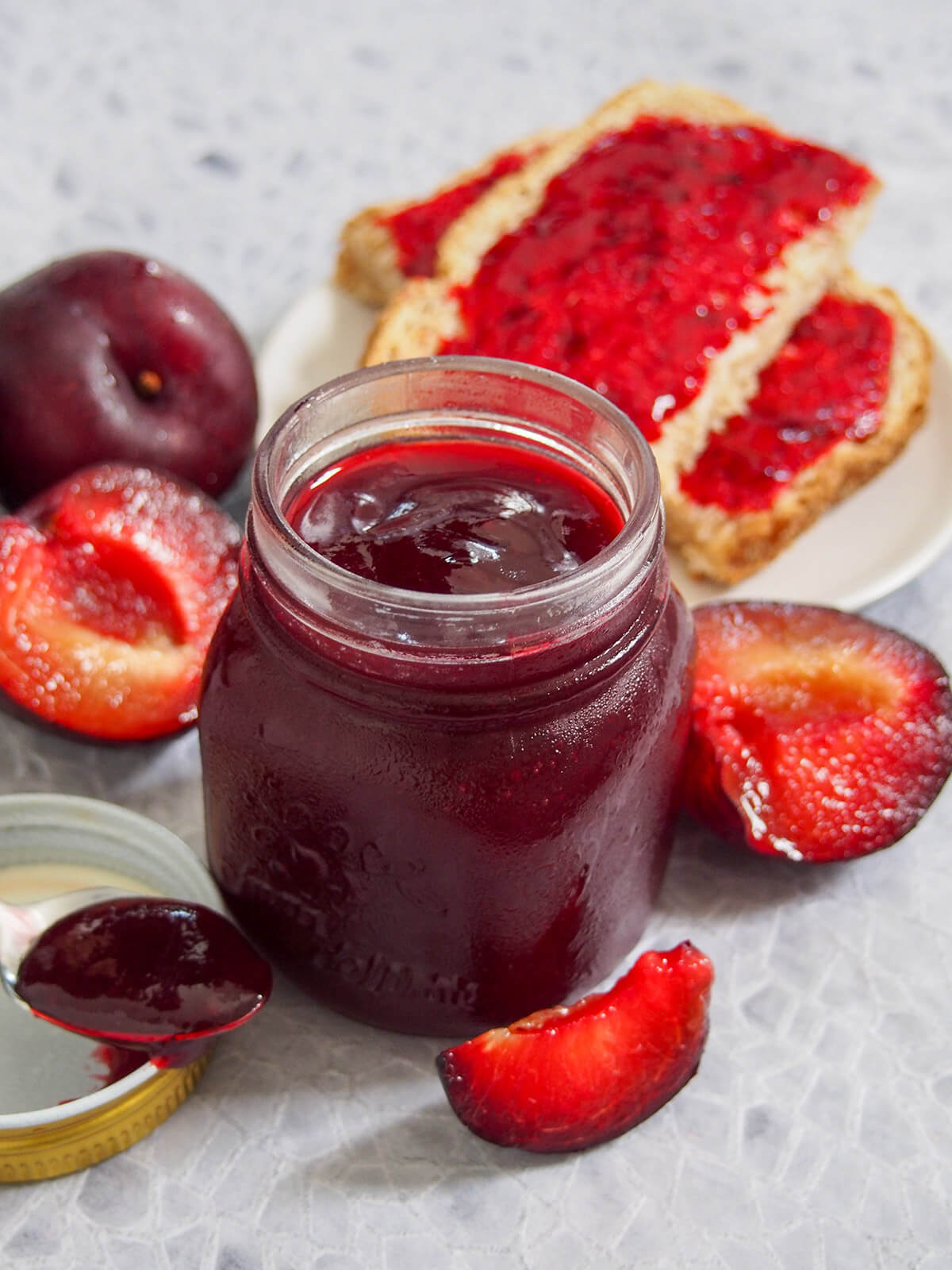 jar of plum jam with pieces of bread with jam behind