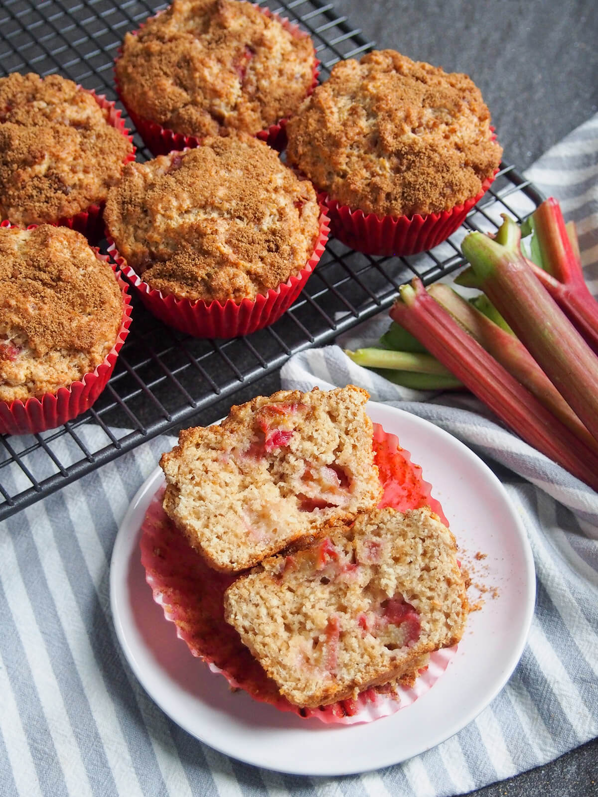 These rhubarb muffins are a delicious combination of tart bursts of rhubarb in a soft muffin and warm sweet cinnamon sugar topping. They make a great coffee time snack, or really any time. sliced open rhubarb muffin in front of more on rack and some rhubarb to side