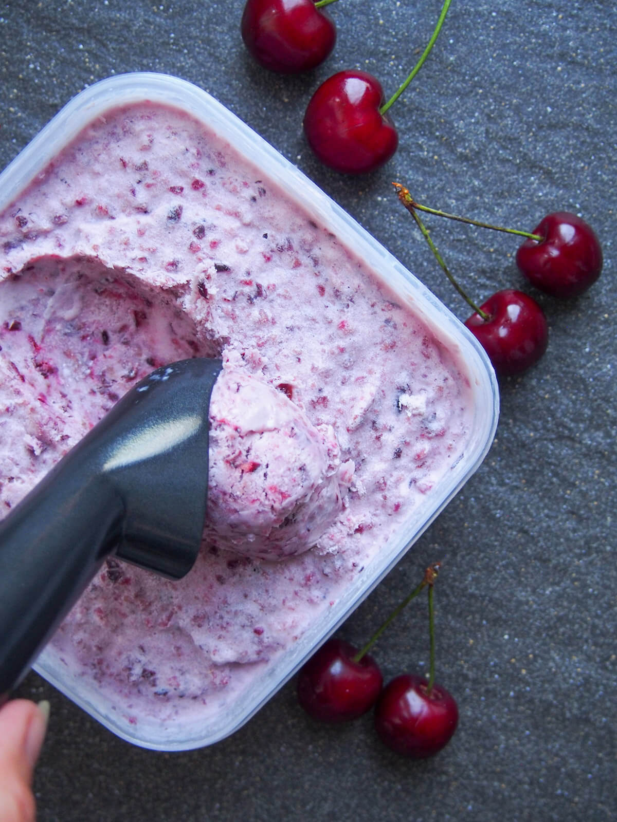 This cherry ice cream is easy to make and packed with wonderfully bright cherry flavor. It uses a simple no churn method that results in a wonderful balance of sweetness, creaminess and fruitiness. scooping cherry ice cream from tub with cherries to side