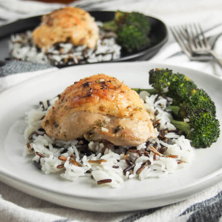 piece of baked tarragon chicken over rice with broccoli to side and second plate behind