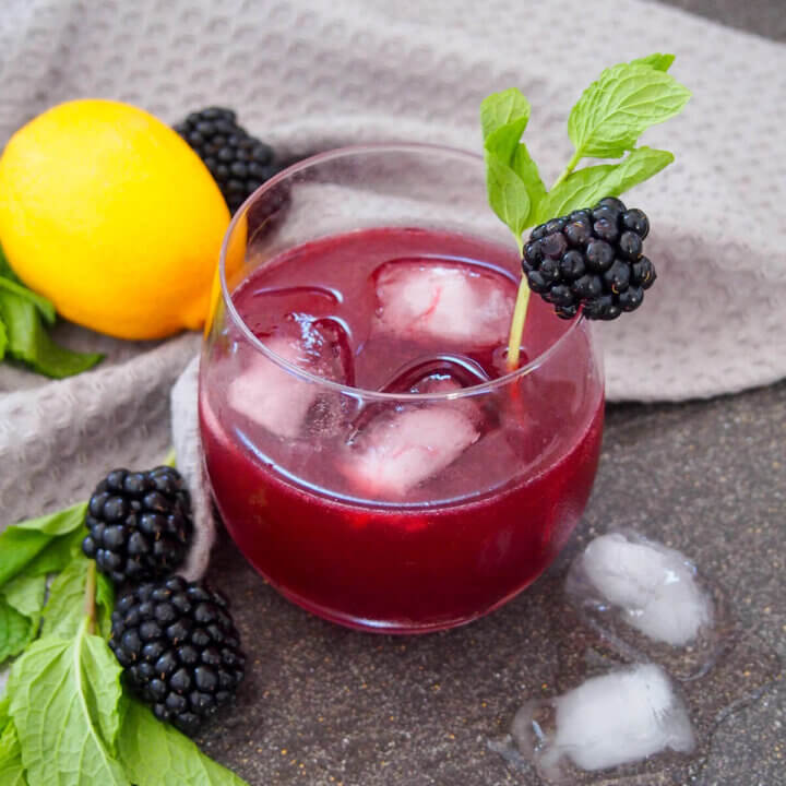 glass of blackberry bourbon smash with lemon and blackberries to side