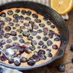 spoon in skillet of blueberry clafoutis