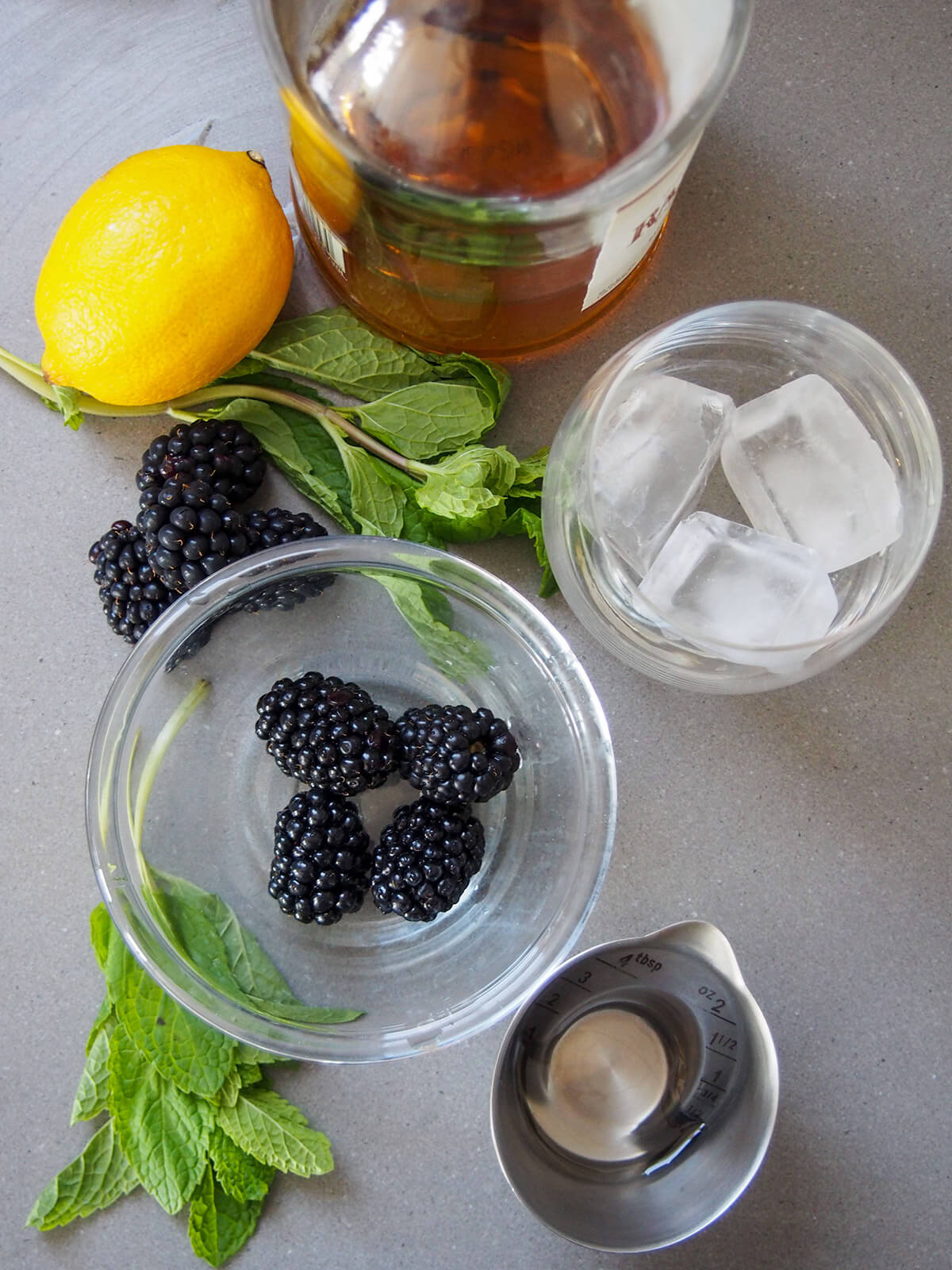 bowls with ice and blackberries with lemon and mint between and bottle of bourbon above