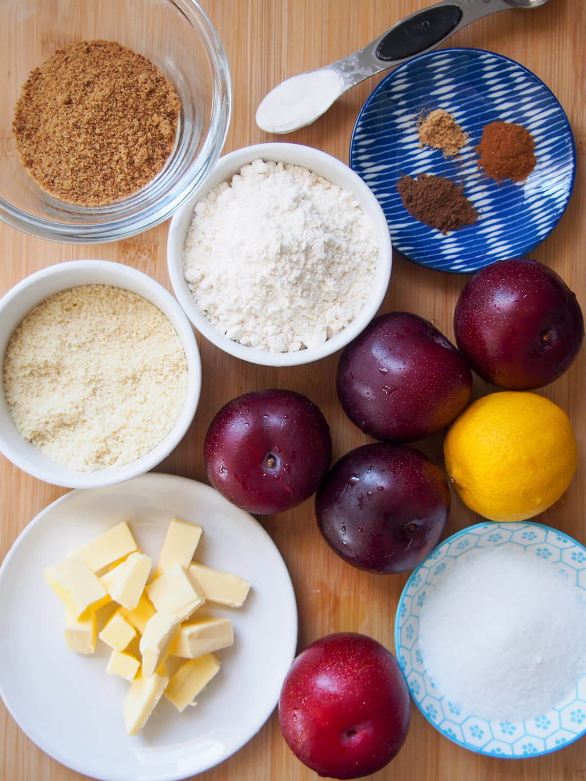 plums on board with bowls with flour, sugars, butter and spices
