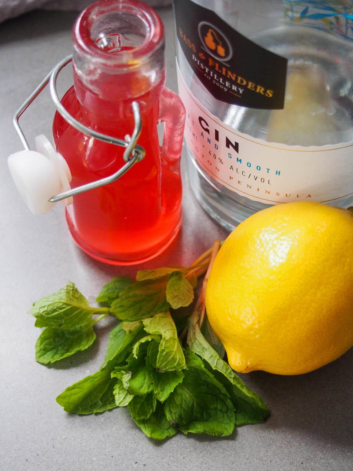 mint, lemon, gin bottle and small bottle with pink syrup