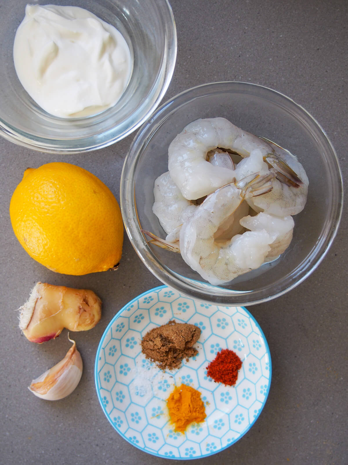 ingredients for tandoori shrimp (prawns) bowl of shrimp, yogurt, spices with lemon, ginger and garlic to side