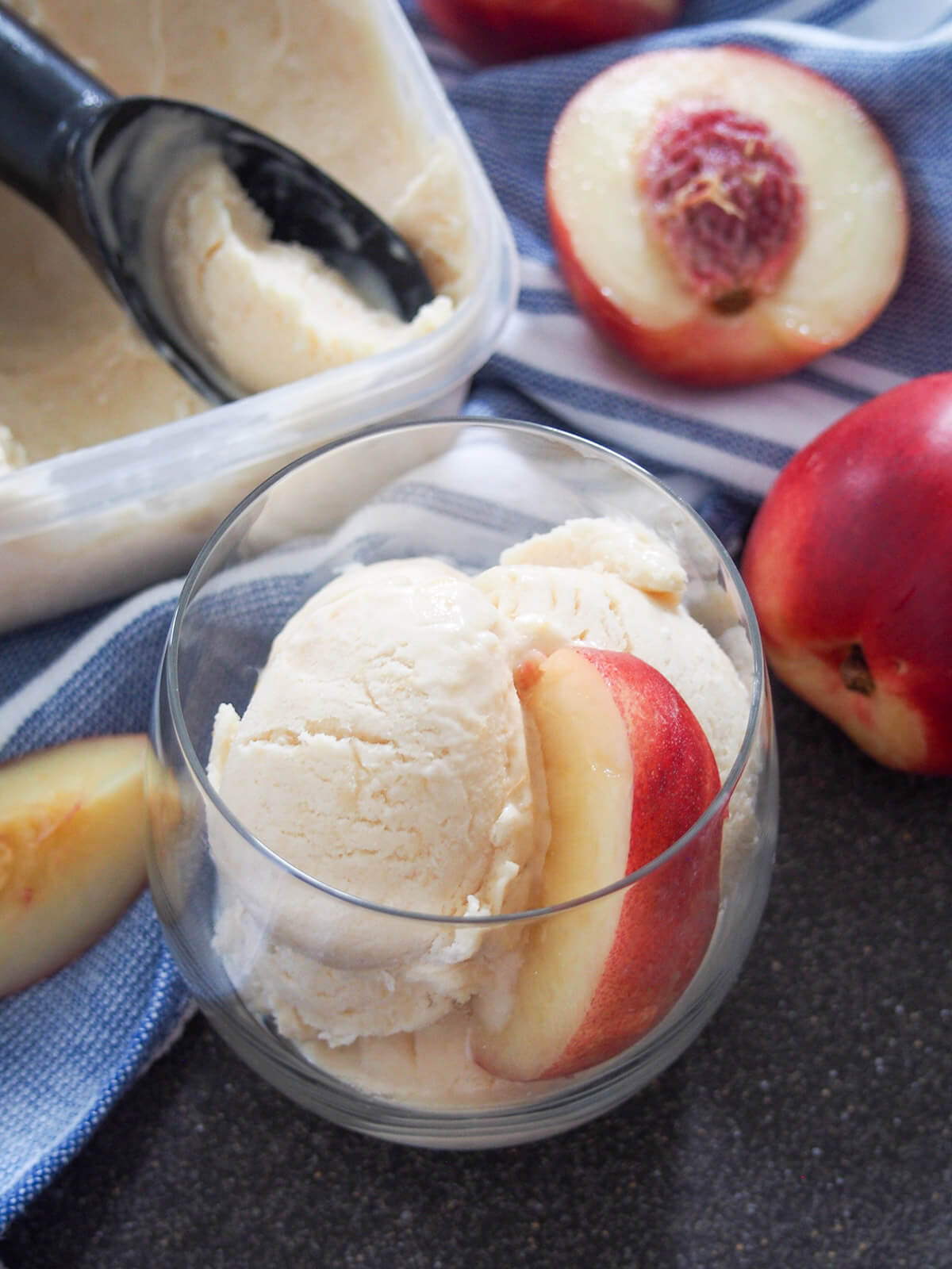 glass of nectarine ice cream with scoop sitting in tub behind