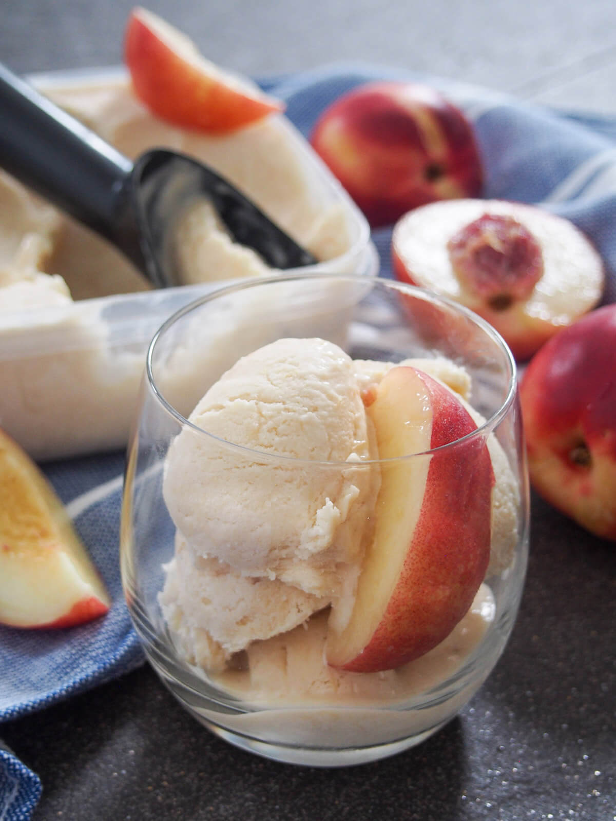 glass of nectarine ice cream from side with scoop sitting in tub behind and pieces of nectarine around