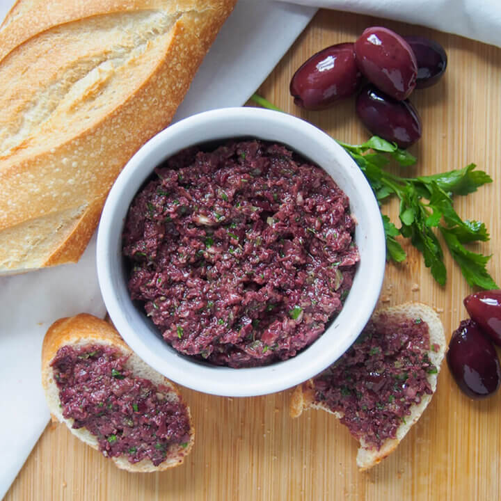 dish of tapenade with olives to one side and bread to other