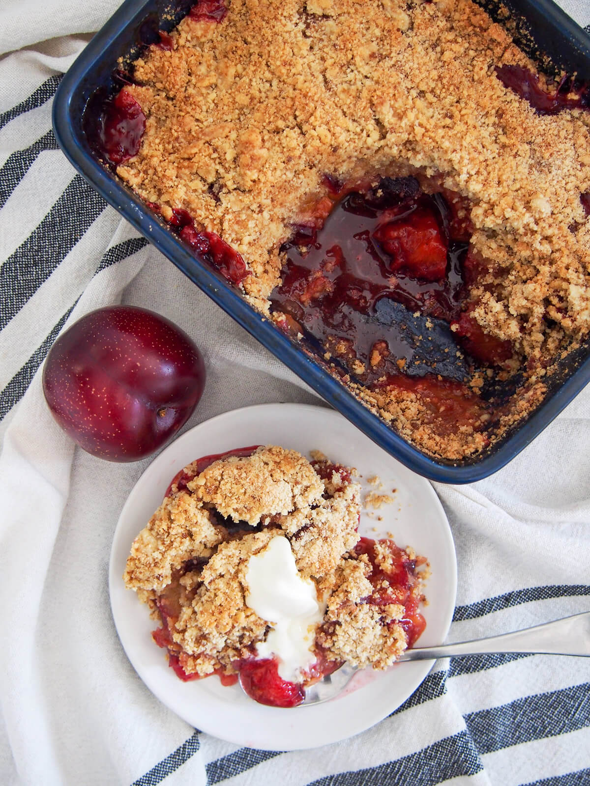 dish of plum crumble with serving taken out on plate below