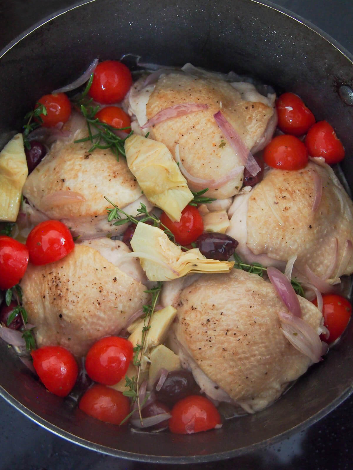 chicken nestled between tomatoes, artichokes, olives and herbs ready for main cook