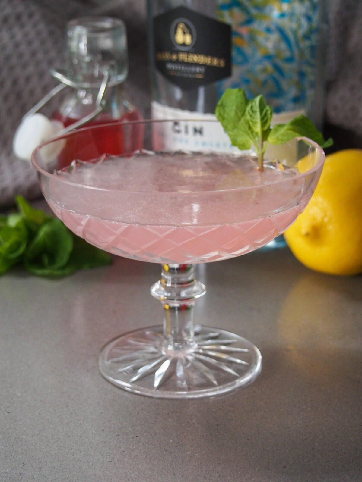 glass of rhubarb southside cocktail with ingredients slightly blurred behind