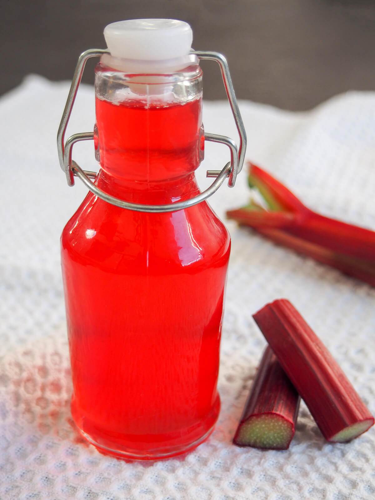 close view of bottle of rhubarb syrup with pieces of rhubarb to side