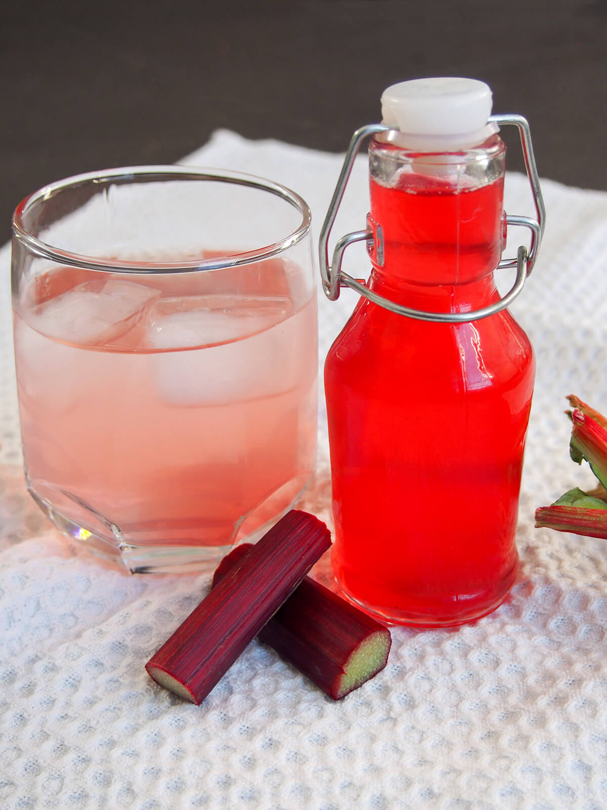 bottle of rhubarb syrup with glass of syrup-infused water to side