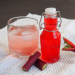 glass with rhubarb syrup mixed with water and jar to side