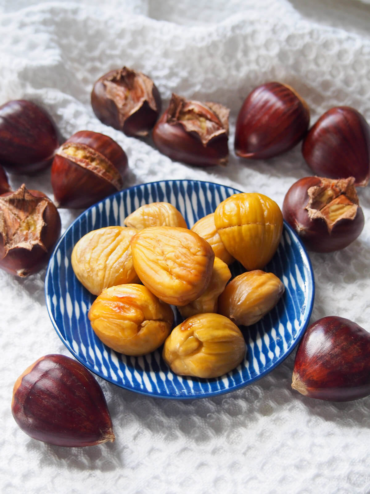 plate of roasted chestnuts with some to peel around and whole chestnuts in front