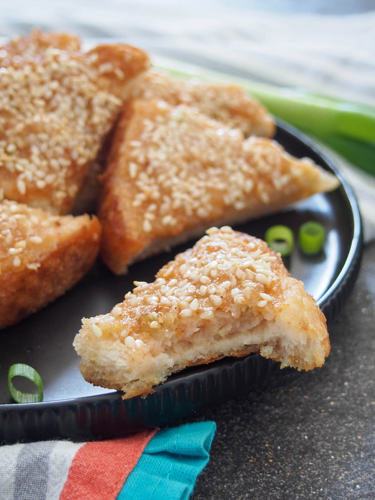 piece of sesame shrimp toast with bite taken from it balancing on edge of plate with more behind