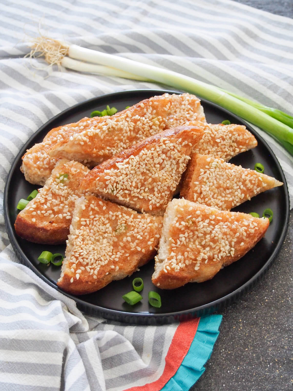 plate of sesame shrimp toast with scallions behind plate