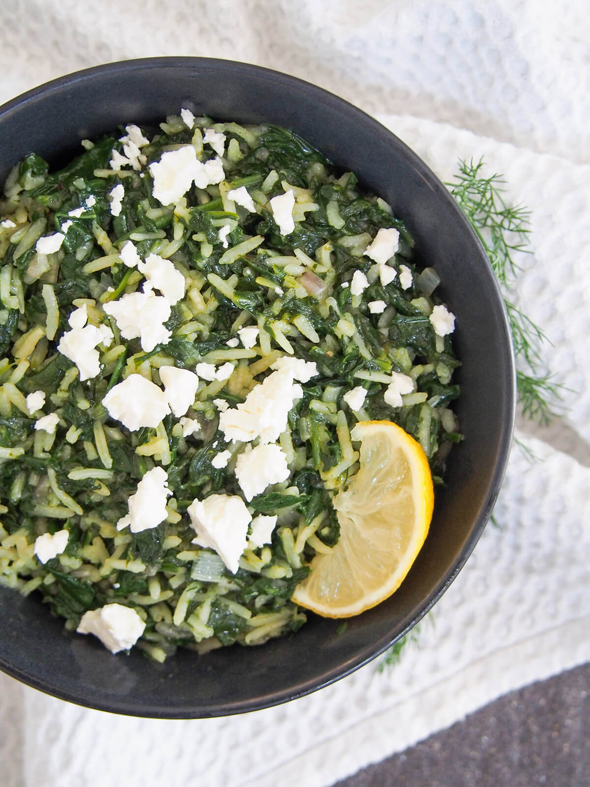 spanakorizo topped with pieces of feta and lemon slice to side