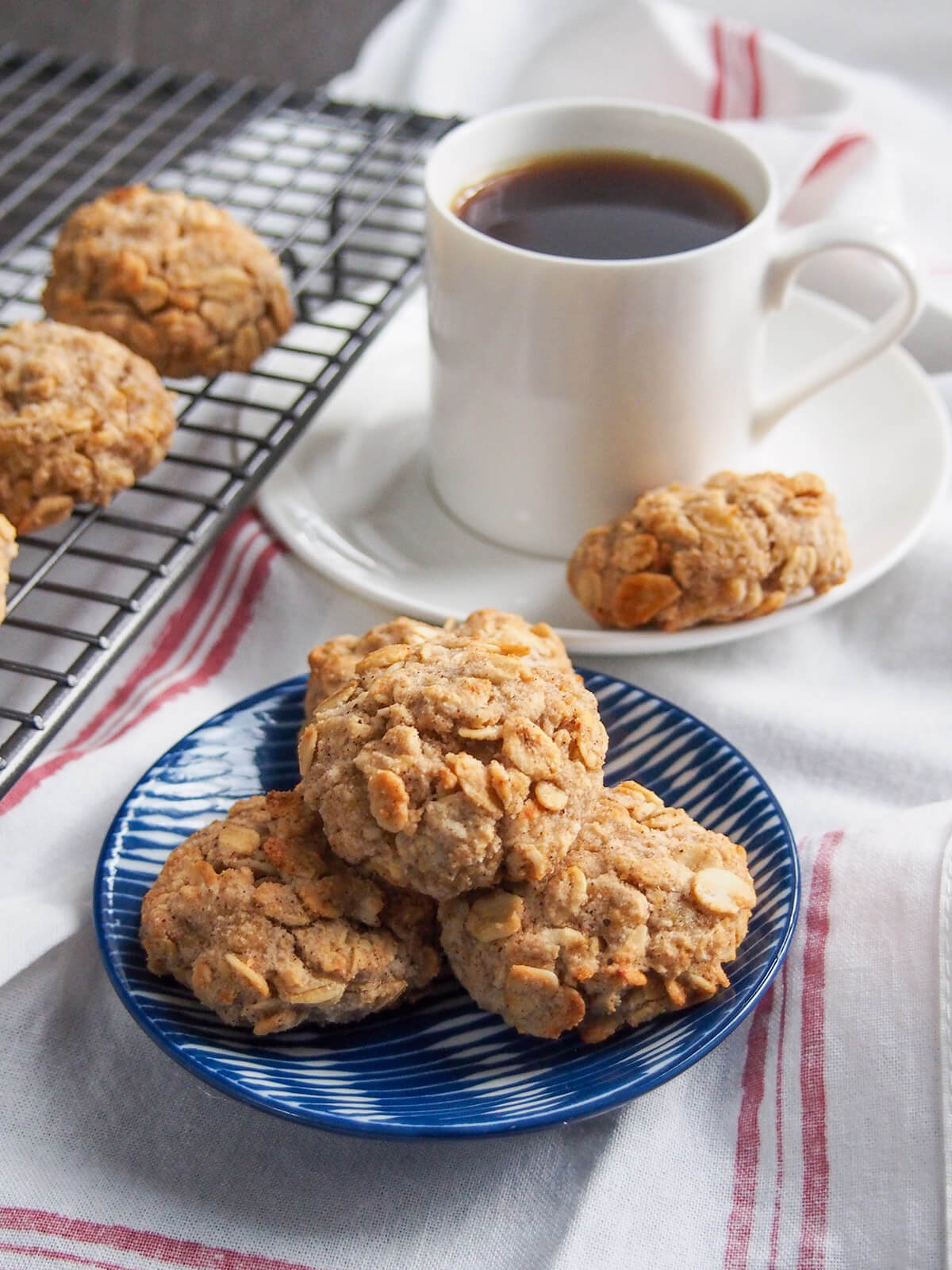 These spiced maple oatmeal cookies are perfect to enjoy some fall flavors, but equally delicious any time. With apple, oats and warm spices, they're deliciously sweet, even being refined sugar free. plate of spiced maple oatmeal cookies with one on saucer in front of coffee cup behind