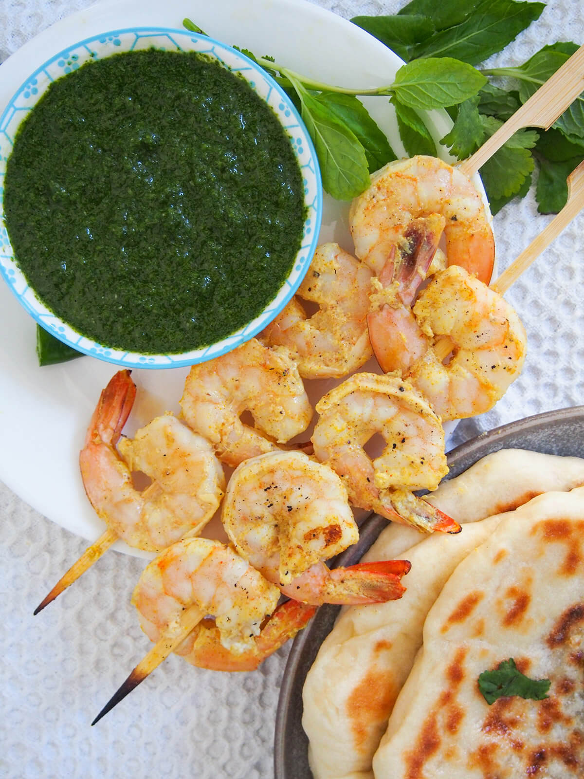 two skewers of tandoori shrimp with bowl of mint chutney to one side and naan to other