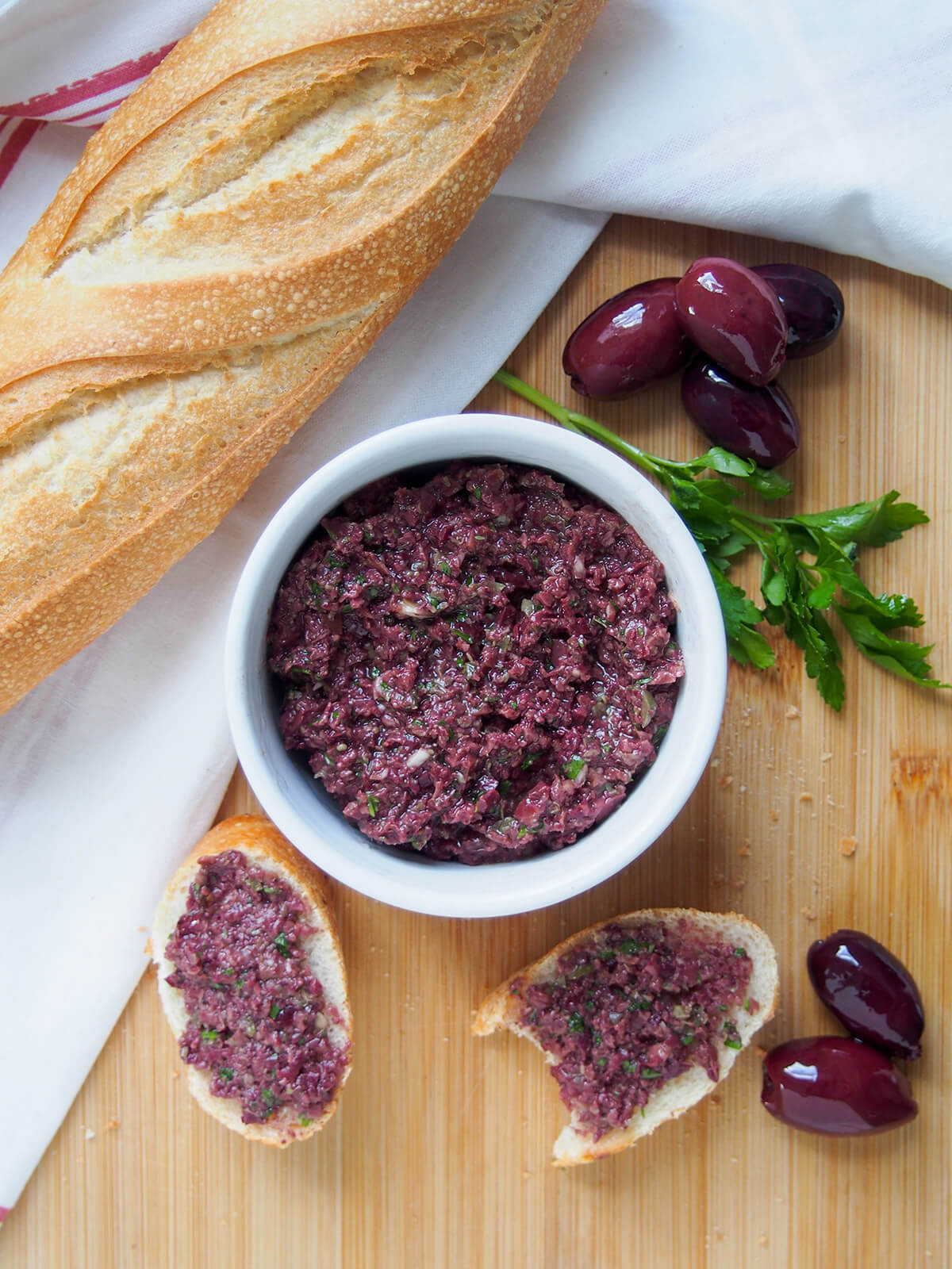 bowl of tapenade with bread to one side and olives to other and some pieces of bread topped with the olive spread below