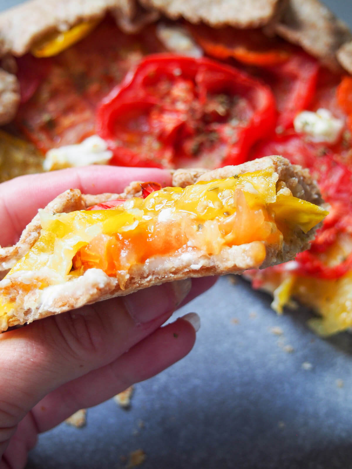 holding a slice of tomato galette in hand with rest of galette behind