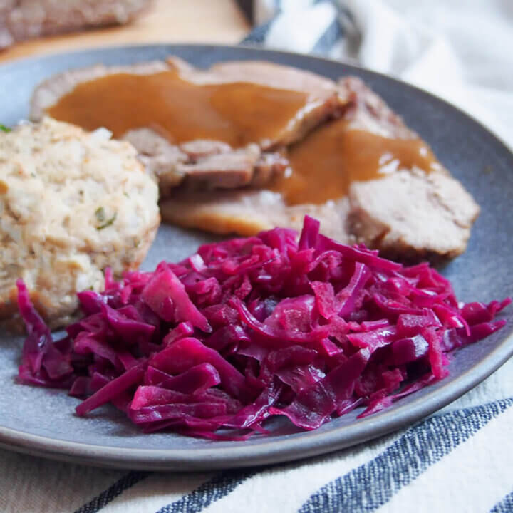 German braised red cabbage in front of pork with gravy and part view of dumpling to side