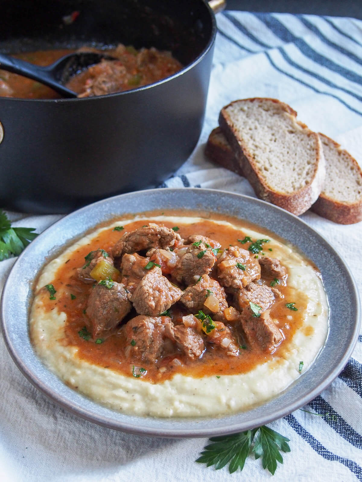 plate of Turkish lamb stew over eggplant bechamel sauce with slices of bread and pot of stew behind