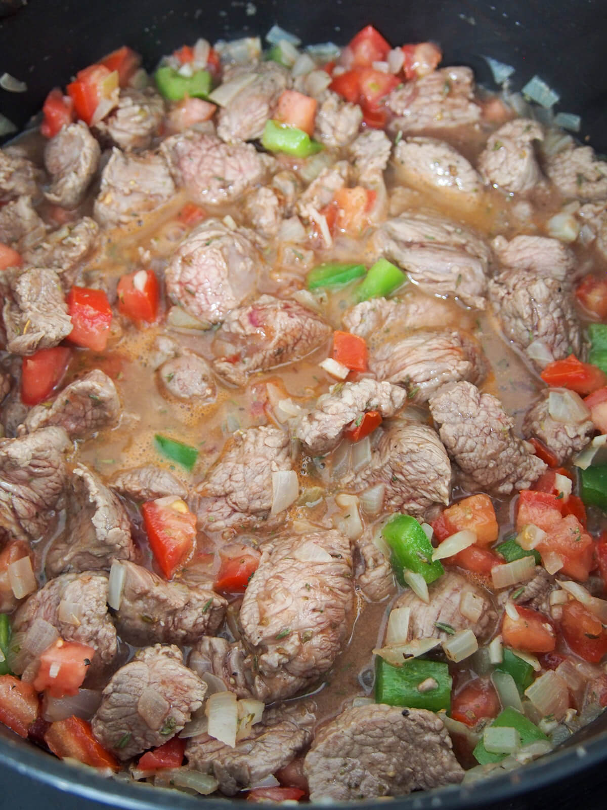 pieces of lamb, tomato and pepper showing in mixture in pot
