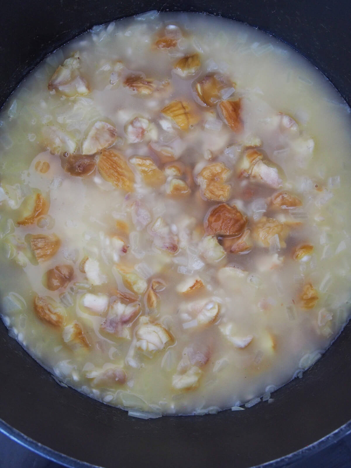 pieces of chestnut showing on top of rice and stock in pan