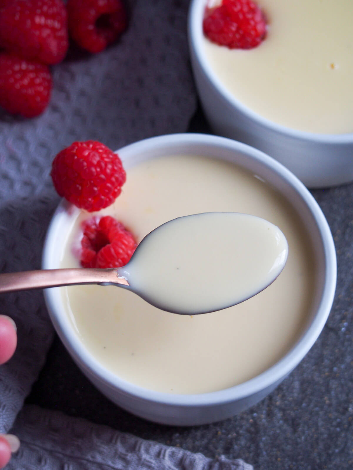 spoonful of creamy sauce held over bowl with more that has raspberries to side