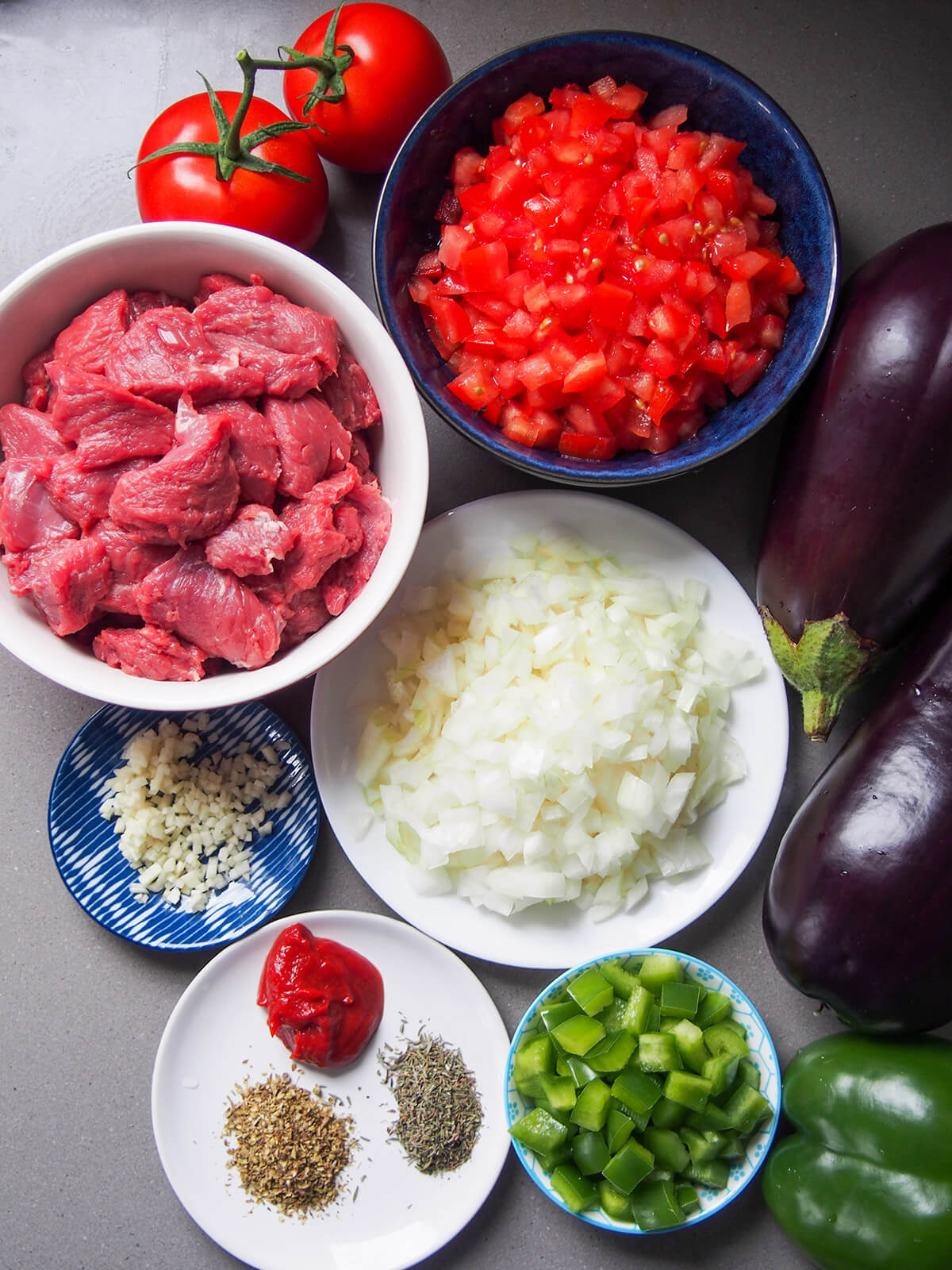 bowls with tomatoes, lamb, onion, pepper, garlic and herbs with eggplant to side