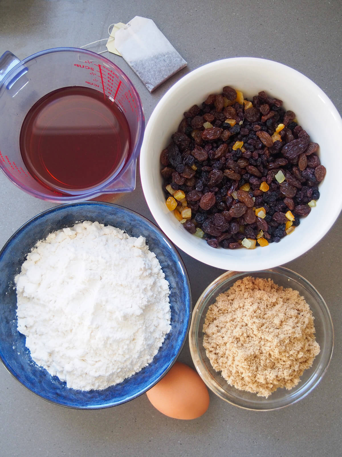 ingredients for Irish brack fruit loaf bowls with fruit, flour, sugar and tea with egg below