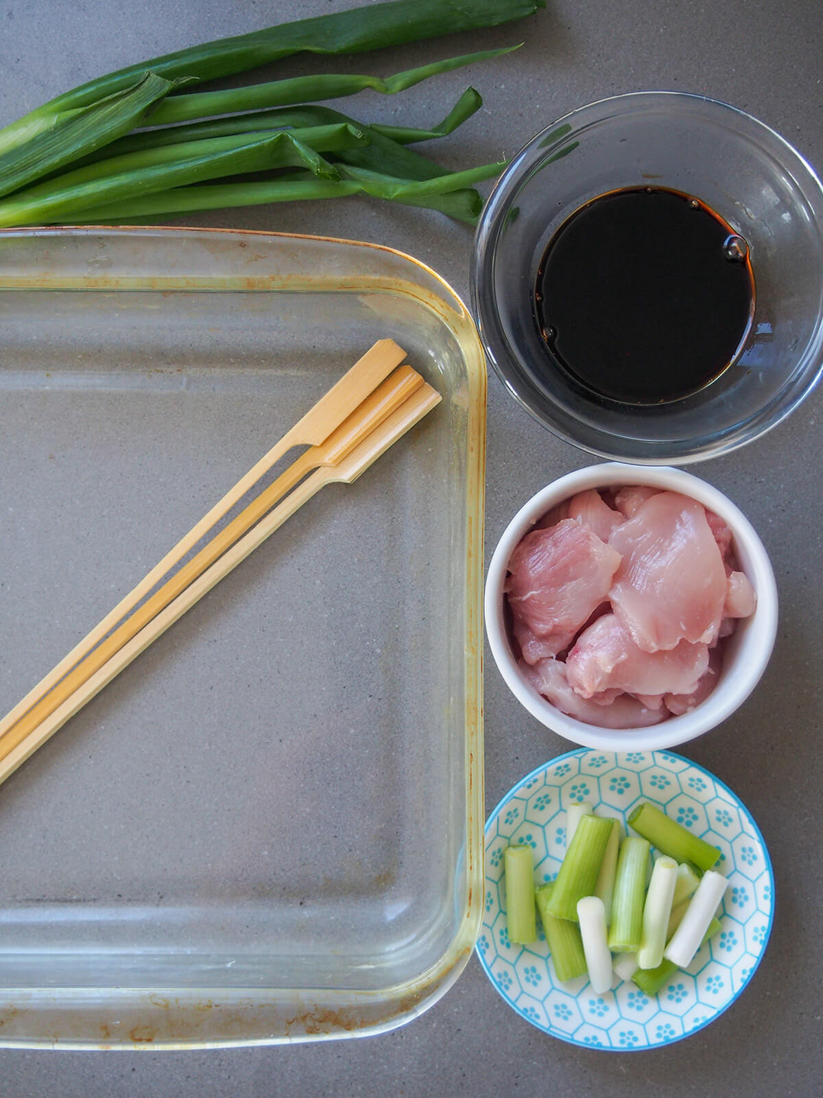 skewers to left and bowls with chicken, spring onion and sauce to right