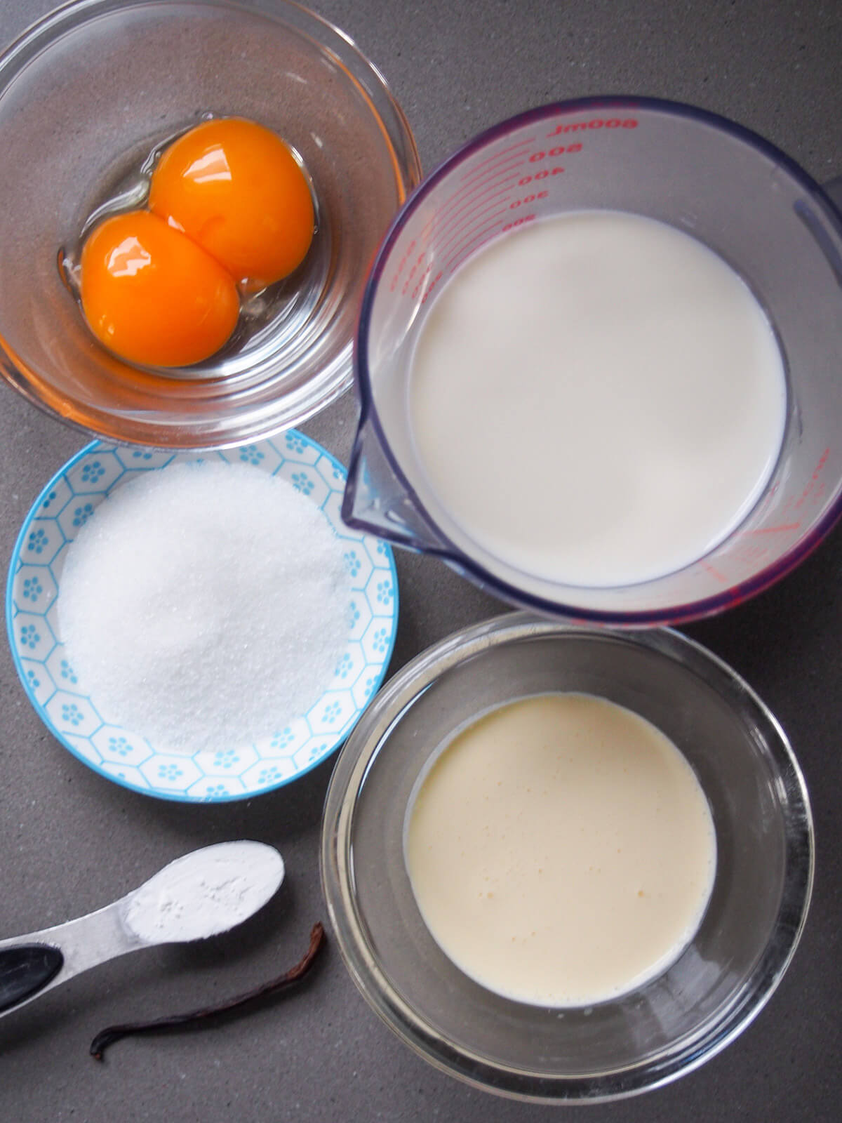bowls with egg yolk, milk, cream, sugar and vanilla