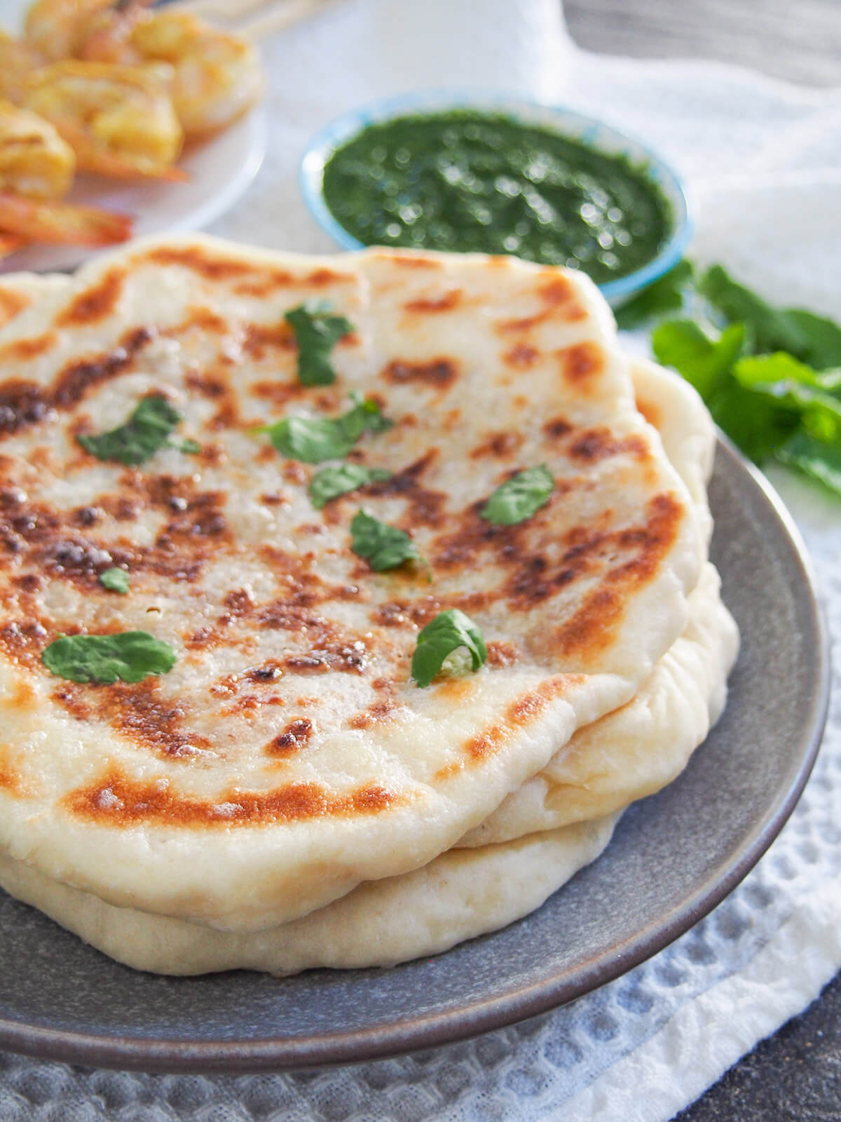 side view of peshwari naan on plate with chutney behind