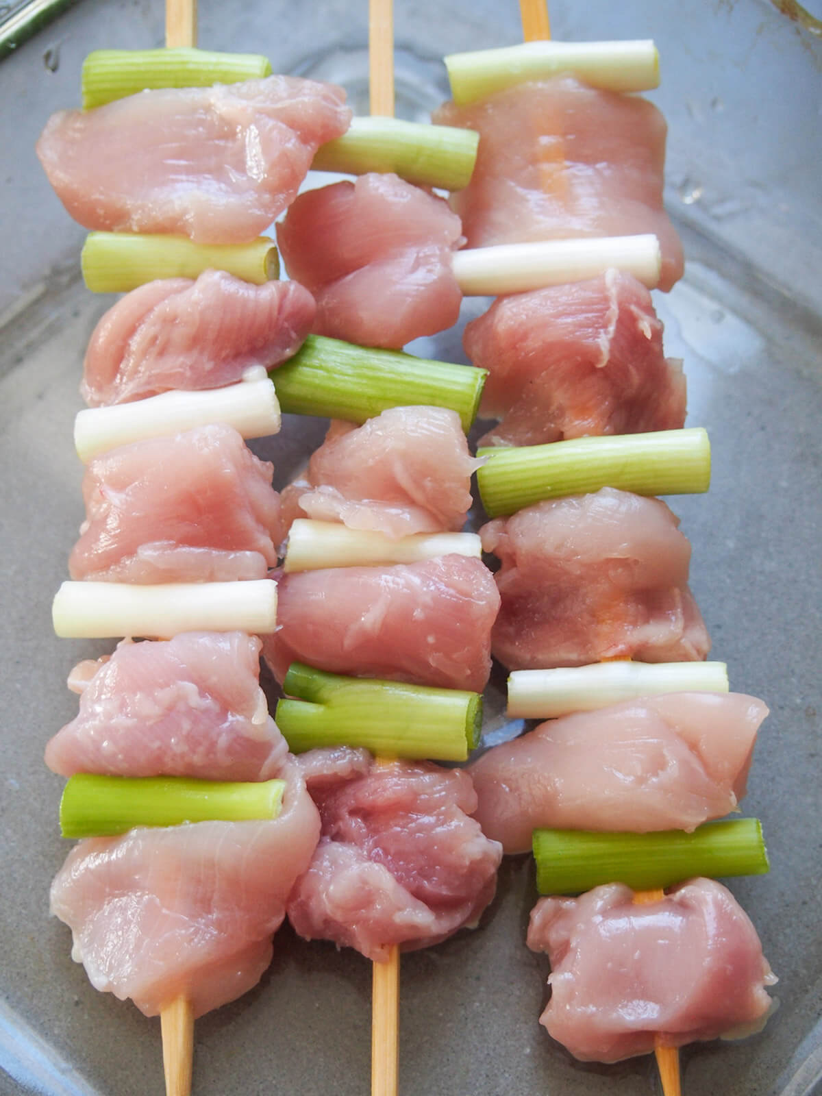skewers with chunks of chicken and spring onion on them before cooking