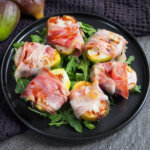 plate of prosciutto wrapped figs on arugula
