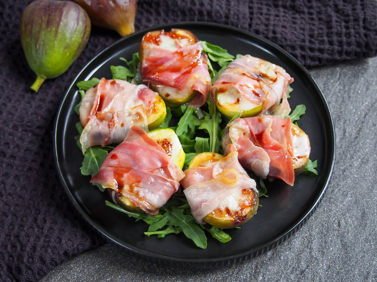 plate with prosciutto wrapped figs sitting on bed of arugula