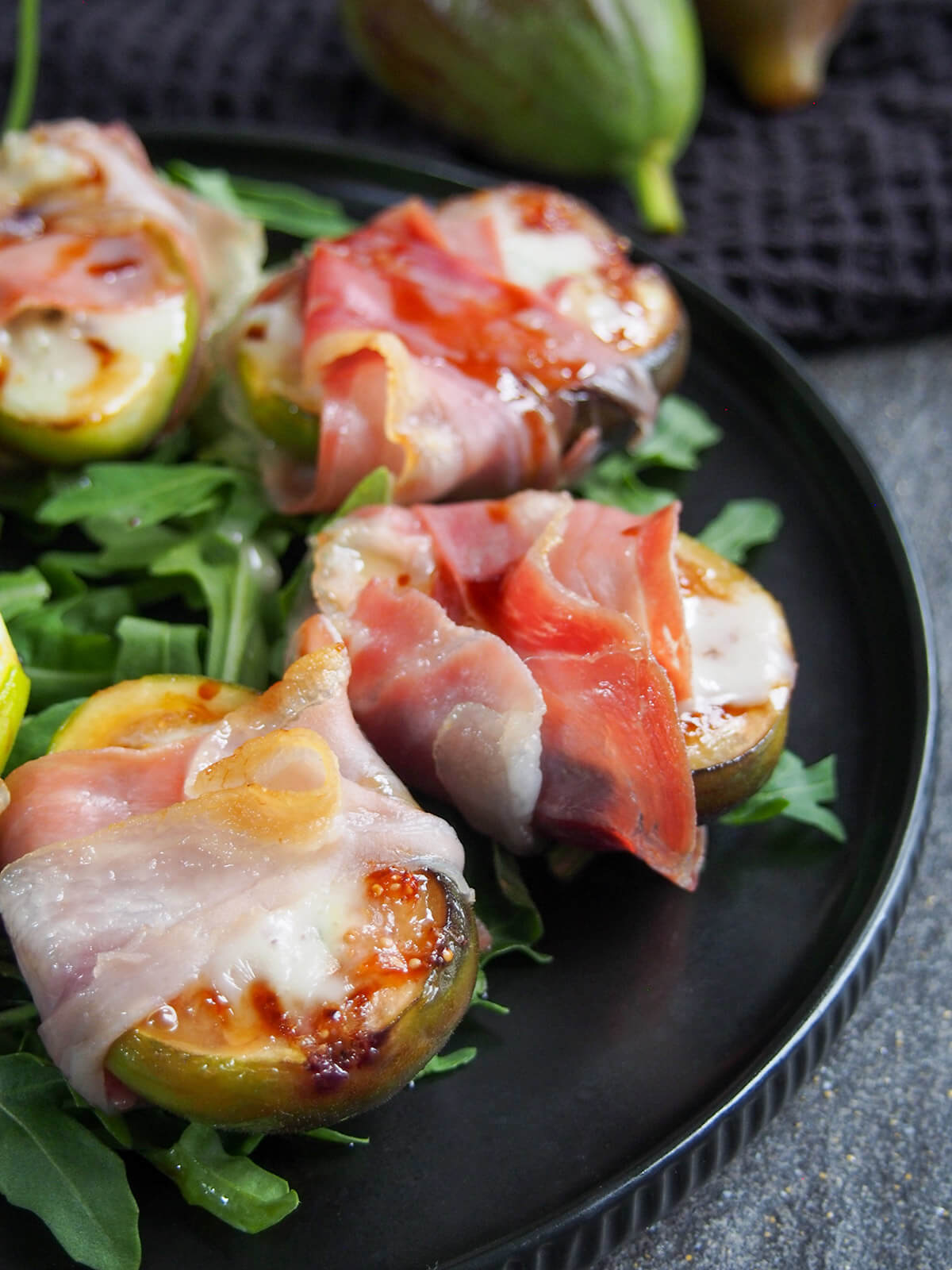 side view of prosciutto wrapped figs on black plate