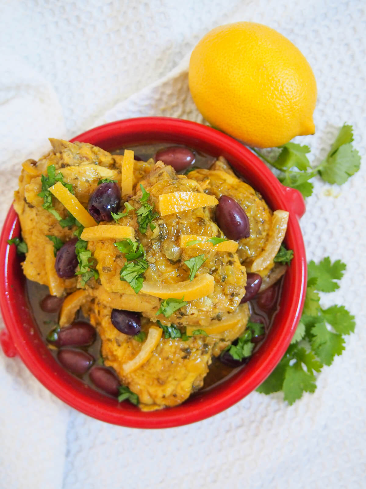dish with pieces of Chicken tagine with preserved lemons and olives with lemon above dish